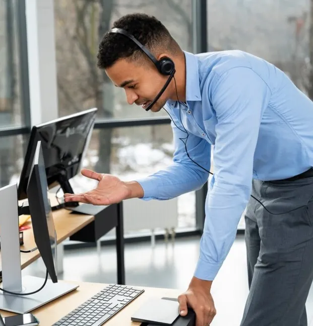 business formation in dubai - Person in a blue shirt gesturing frustration towards a computer monitor at a desk.