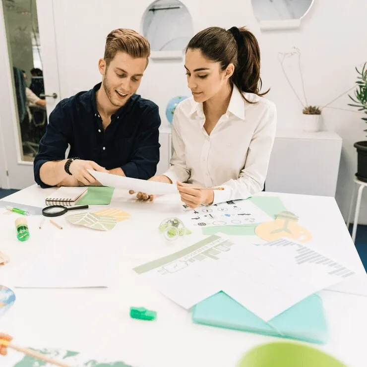  Freezone - Two people discussing papers on a desk with office supplies and charts.