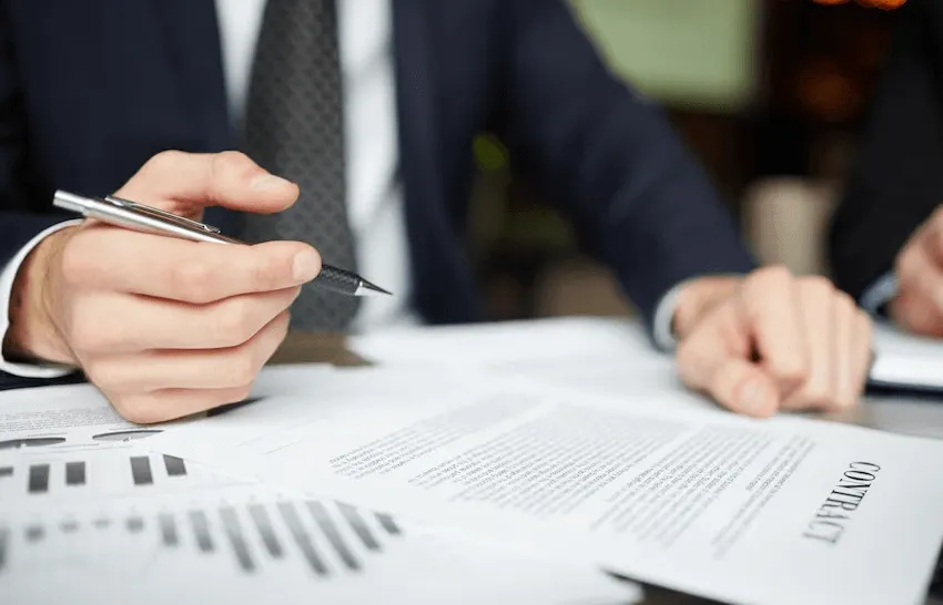 business setup services in uae -Businessperson holding a pen over documents with charts and text during a meeting.